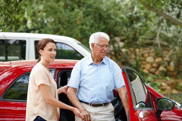 Caregiver assisting a senior man with a walker out of a car at a medical appointment in Raleigh North Carolina